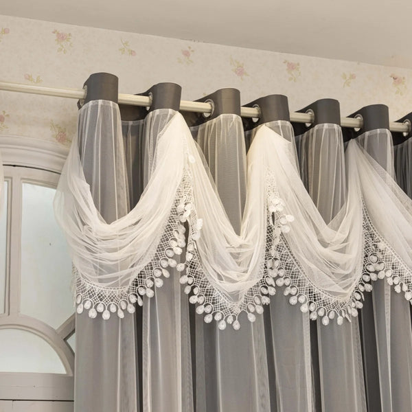 Gray sheer curtains with white lace trim hanging on a rod against a light-colored wall.