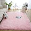 A pink plush long-pile area rug is displayed on a light wooden floor in a bright living room setting.