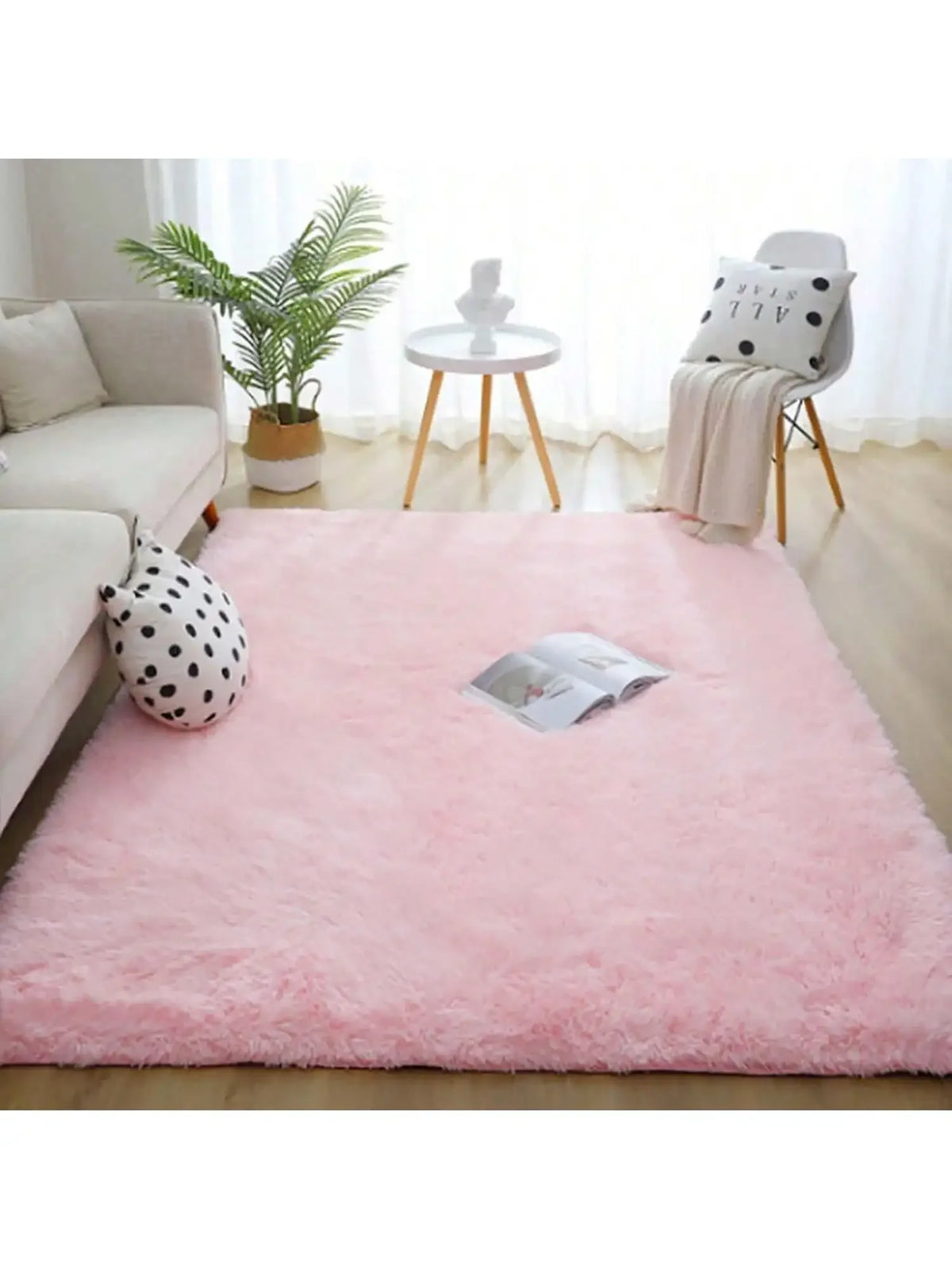 A pink plush long-pile area rug is displayed on a light wooden floor in a bright living room setting.