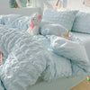 A light blue soft textured duvet cover set with matching pillowcases and a pink stuffed animal on a bed.