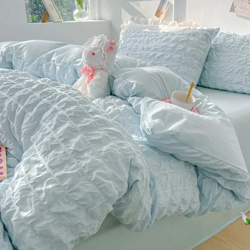 A light blue soft textured duvet cover set with matching pillowcases and a pink stuffed animal on a bed.