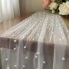 A sheer white tulle table runner adorned with small pearl beads and draped elegantly on a wooden surface.