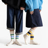 A person wearing dark denim pants and a black sweater is holding the hands of another person wearing a light blue top and a d
