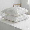 A stack of pure white Princess Ruffle Cotton bedding pillows on a white surface.