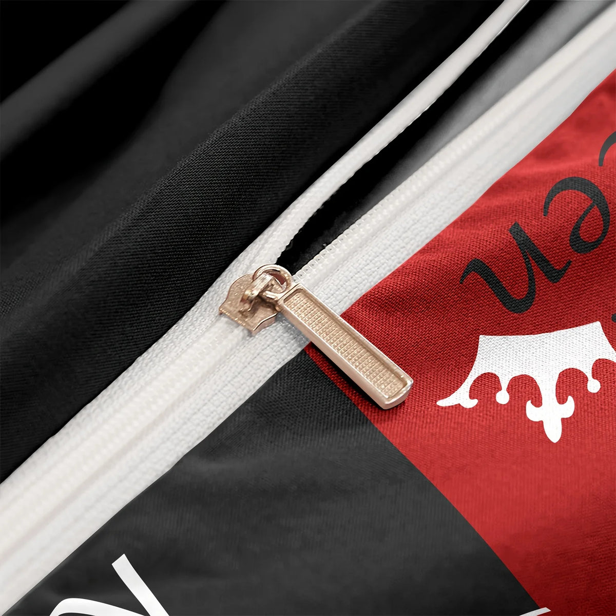 A close-up of a zipper on dark red and black printed letter bedding fabric with a gold-toned zipper pull.