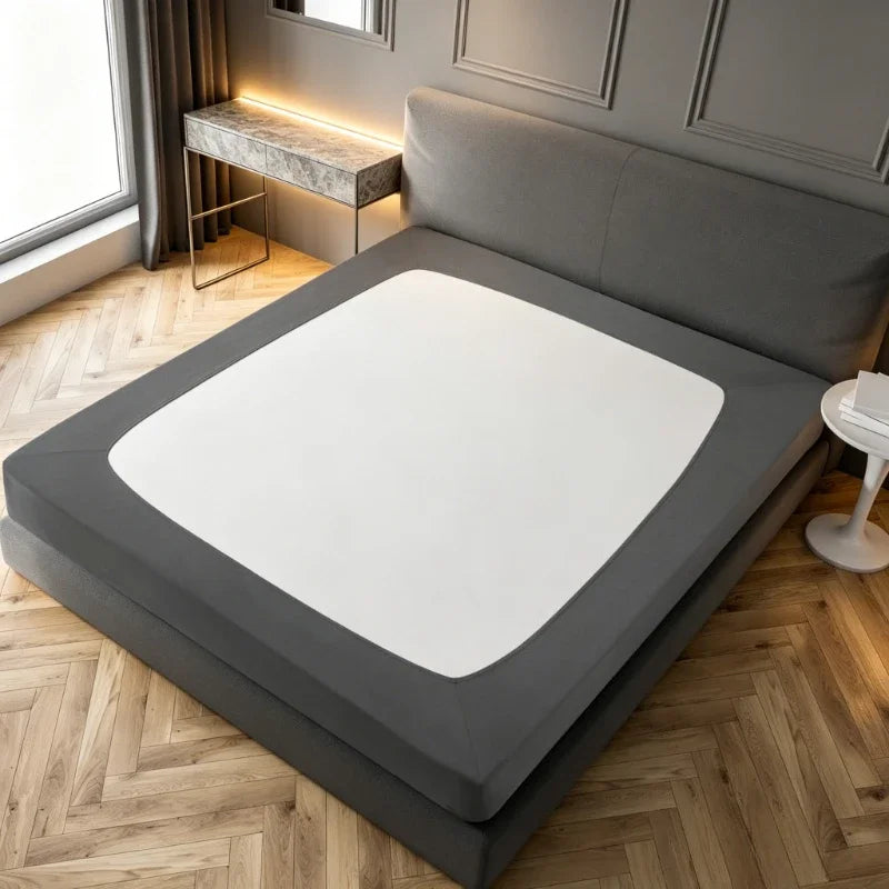 A gray box spring protector cover lying on a wooden floor next to a window.