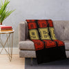 A knitted throw blanket with bold orange and black lettering draped over a gray sofa.