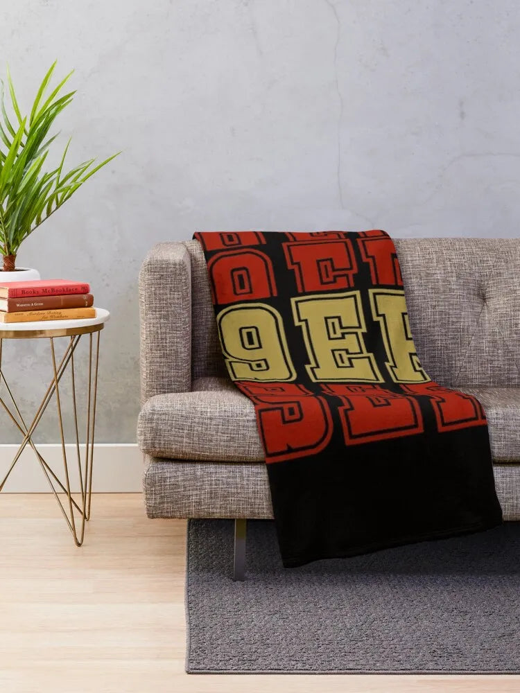 A knitted throw blanket with bold orange and black lettering draped over a gray sofa.