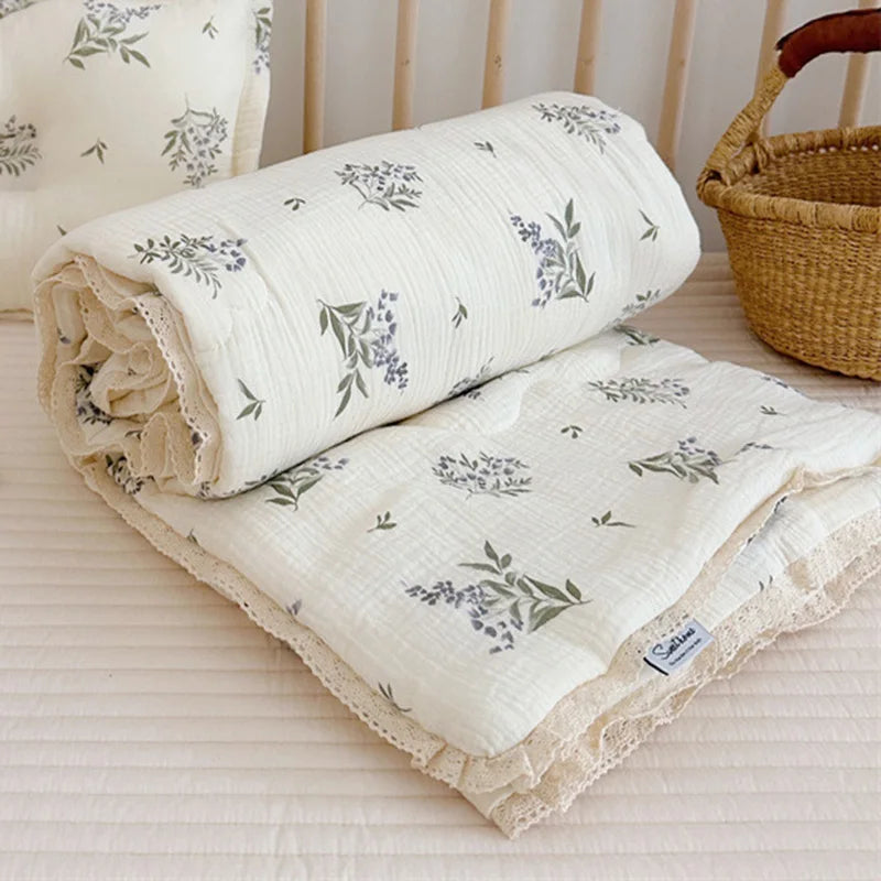 A rolled white muslin blanket with a soft floral print is displayed next to a woven basket.