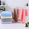 A set of ten luxury coral velvet cleaning face towels in various pastel shades stacked next to a wooden tray.