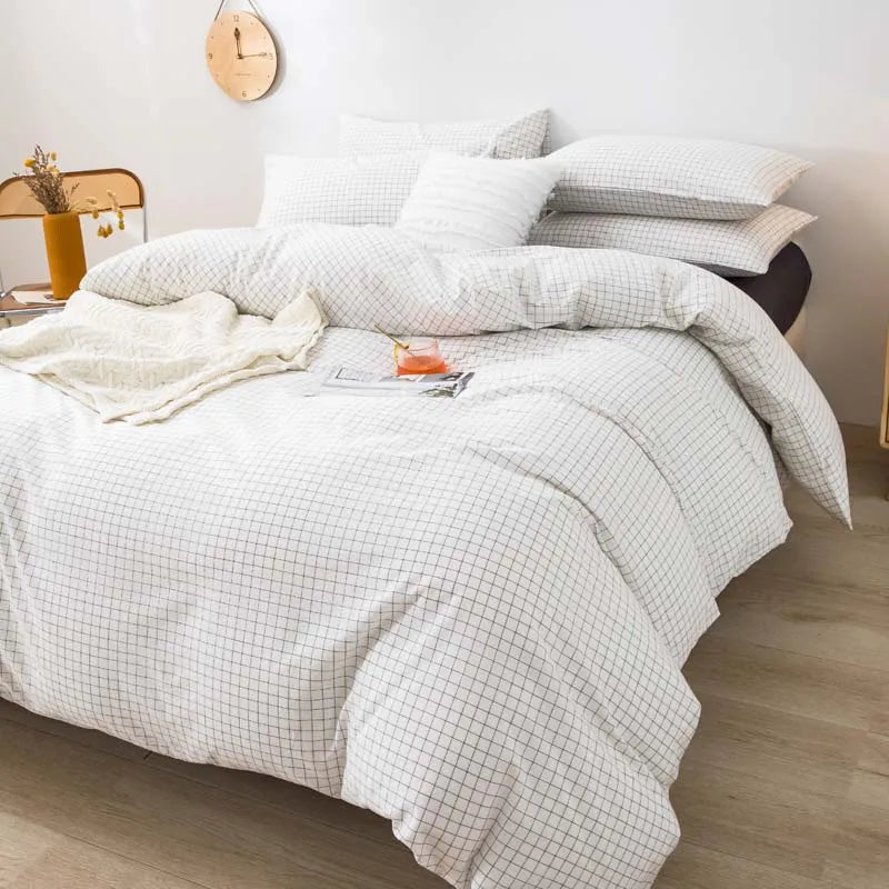 A set of three white plaid duvet covers and pillowcases neatly folded on a bed.