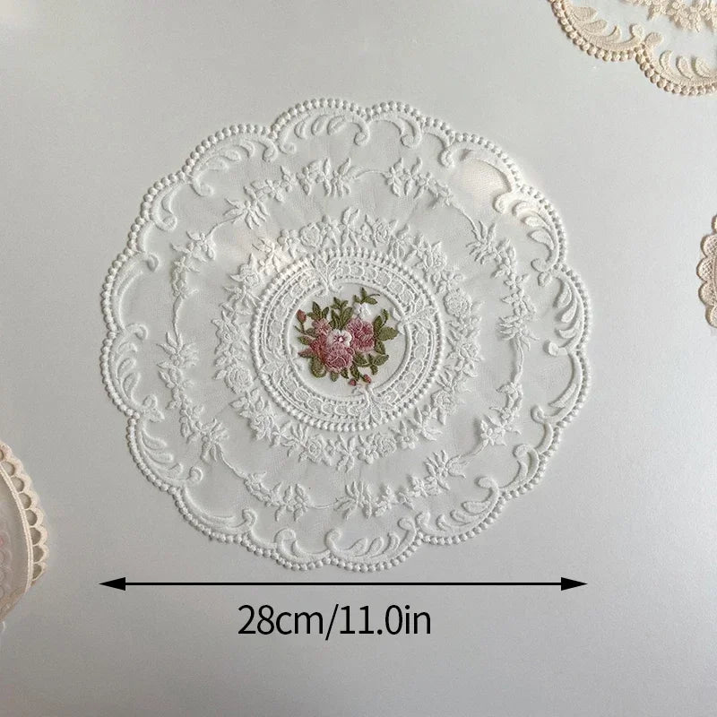 White oval lace embroidered coaster with a pink floral design on a light background