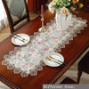Elegant jacquard lace table runner displayed on a wooden table with place settings and floral arrangement.