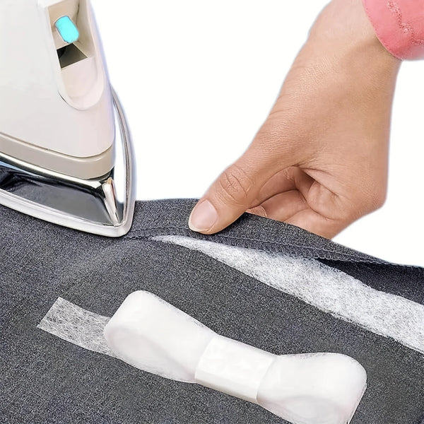 A hand is applying iron-on fusible hem tape to a piece of dark gray fabric for DIY sewing.
