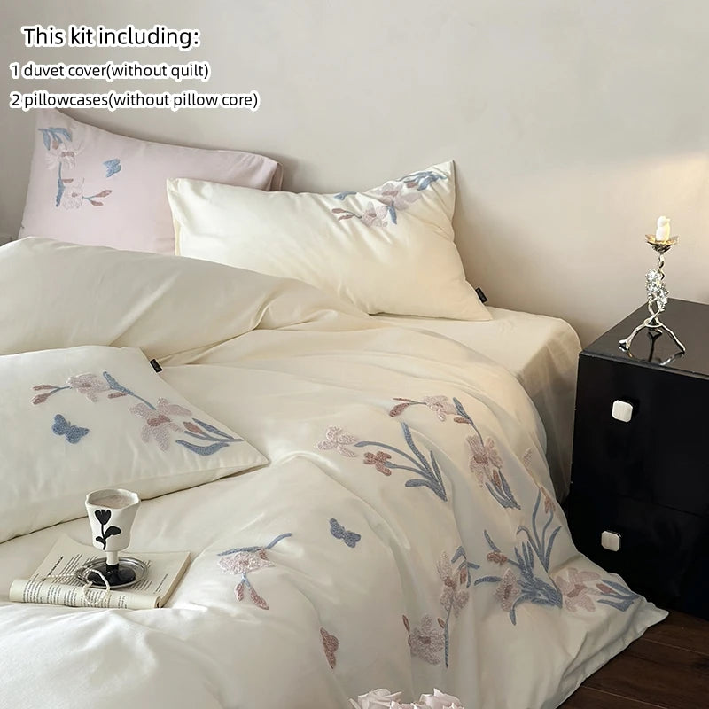 A set of embroidered orchid duvet cover and pillowcases in white with lace trim displayed on a bed.