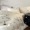 A set of embroidered orchid duvet cover and pillowcases in white with lace trim displayed on a bed.