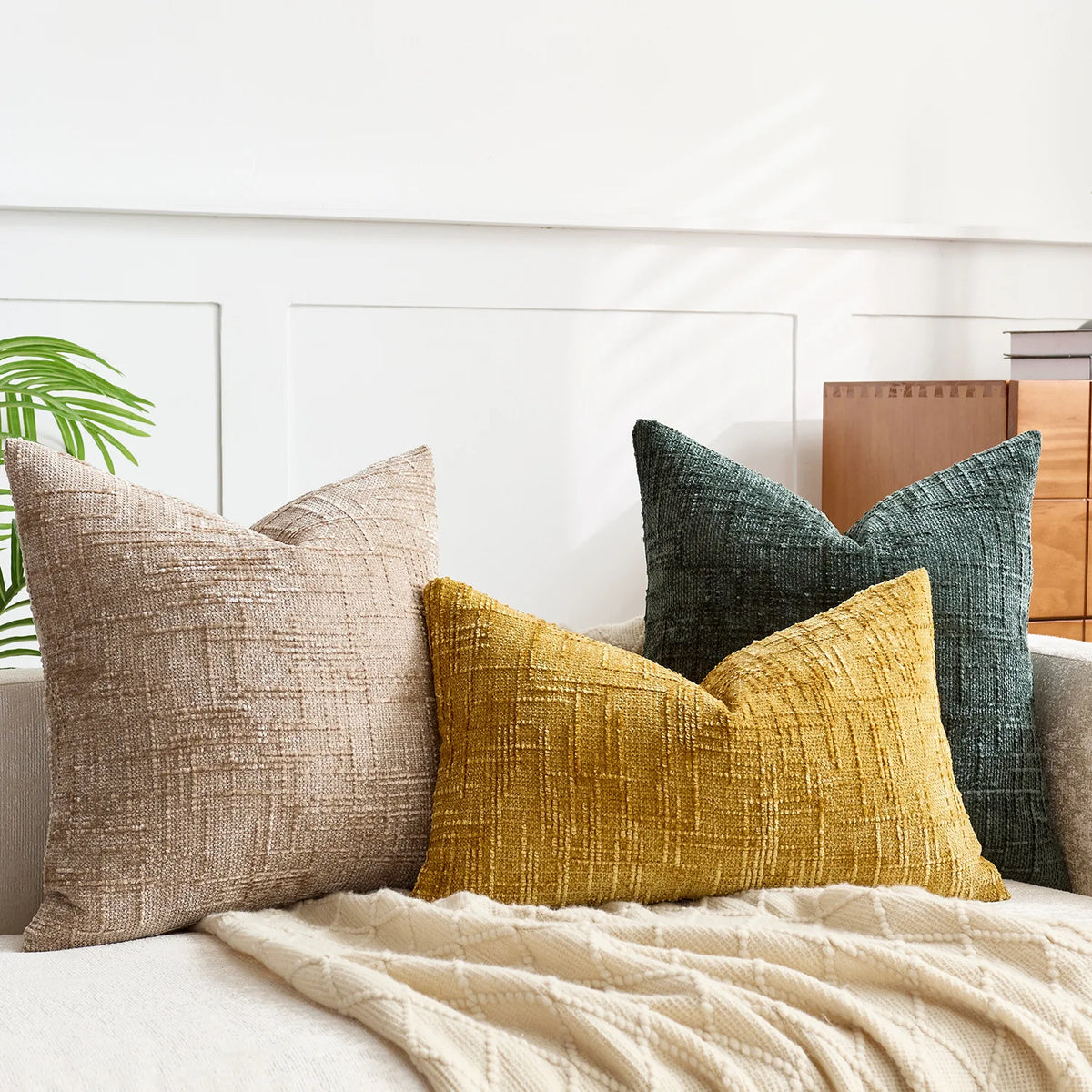 A collection of textured throw pillows in beige, mustard yellow, and dark green fabric on a light sofa.