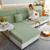 A light green jacquard elastic sofa slipcover with a white knitted sweater and orange accent pillows.