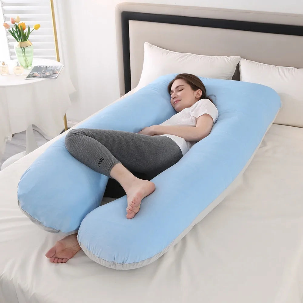 A woman rests on a light blue U-shaped maternity body pillow on a white bed.