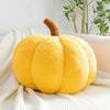 A bright yellow fuzzy pumpkin plush decoration with a brown stem resting on a white knitted fabric.