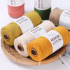 Rolls of hand-knitted cotton yarn in various colors including pink, green, beige, and yellow on a wooden tray