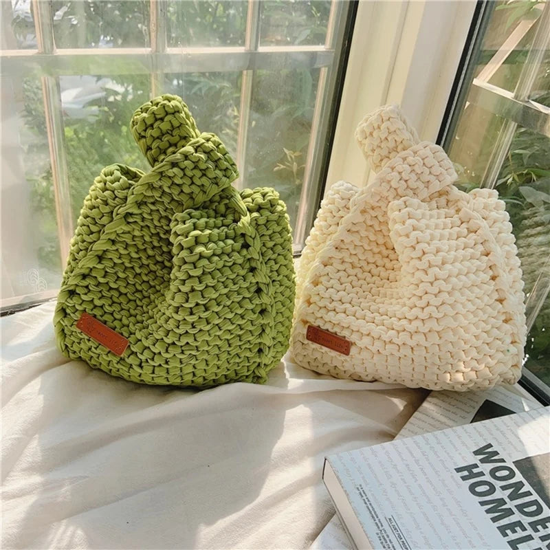 A handmade crochet bag in bright lime green sits on a windowsill next to a cream-colored bag.