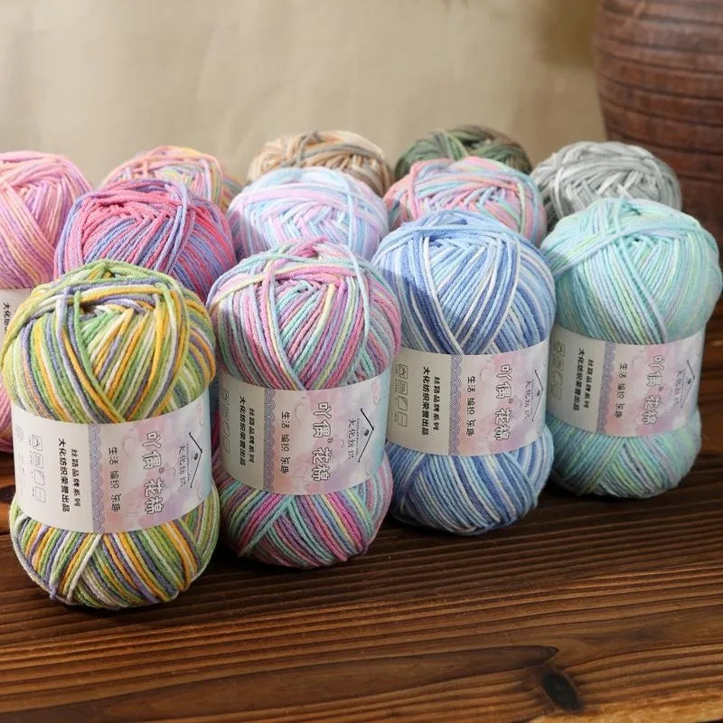 A collection of multicolored 4-ply cotton knit yarn skeins in various shades and textures arranged on a wooden surface.