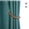 A close-up of a copper rope tieback clip used to secure a teal curtain, shown against a soft fabric background.