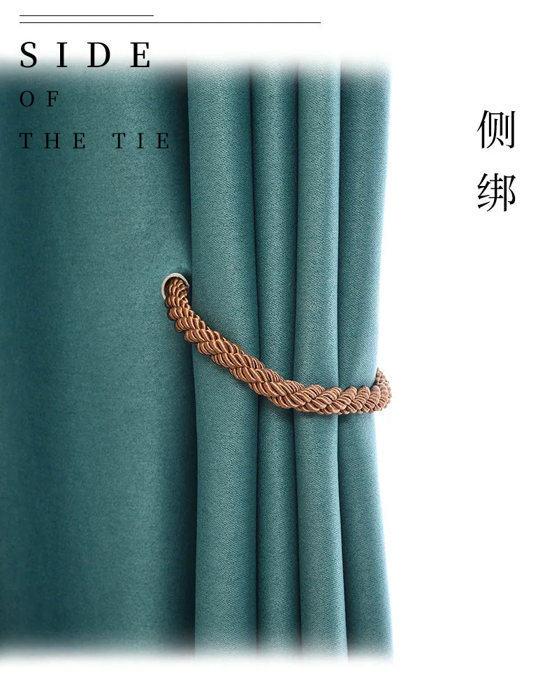 A close-up of a copper rope tieback clip used to secure a teal curtain, shown against a soft fabric background.
