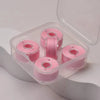 A clear plastic container holds several pink prewound sewing machine bobbin threads.