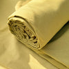 A rolled light yellow organic cotton flat sheet and pillowcases on a beige background.