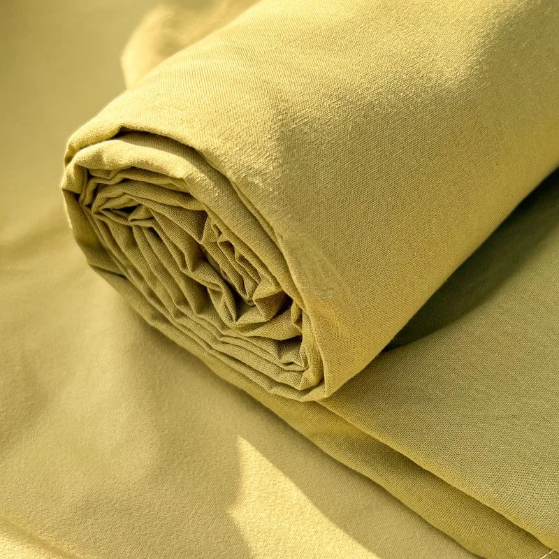 A rolled light yellow organic cotton flat sheet and pillowcases on a beige background.