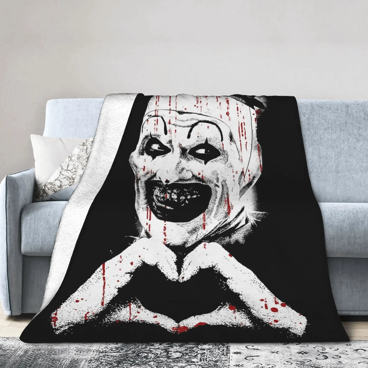 A black and white graphic featuring a menacing clown face with blood splatters on a plush coral fleece throw blanket.