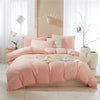 A pink duvet cover set with pom-pom decoration displayed on a bed against a light wall and white curtains.