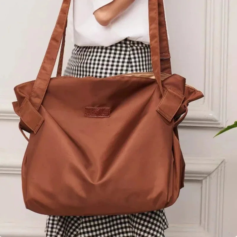 A brown foldable tote bag with leather straps is shown against a white and black checkered skirt.