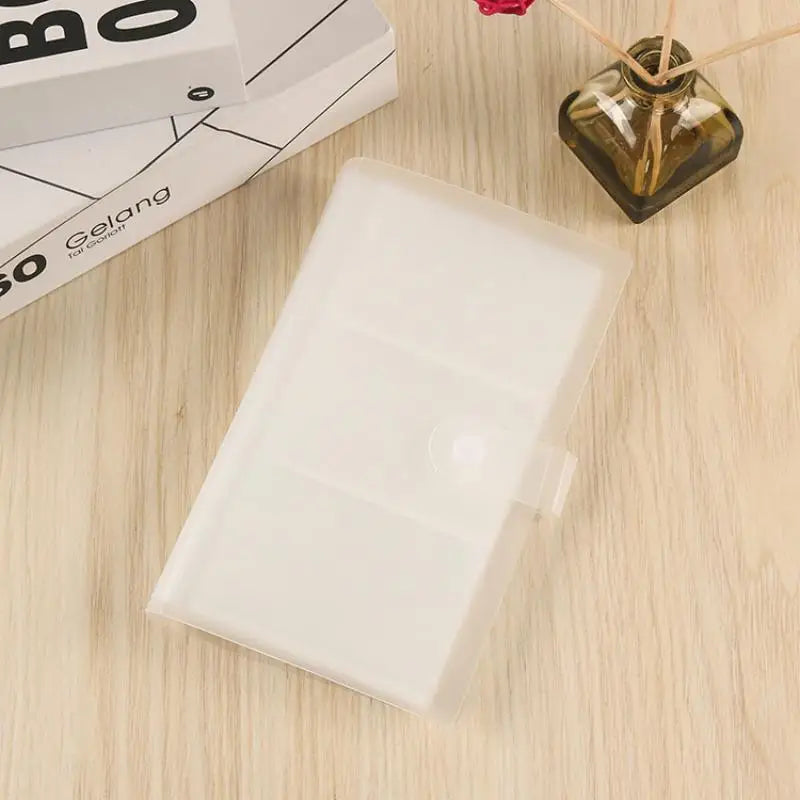 A clear plastic photo storage card album resting on a wooden surface next to a box and a glass jar.
