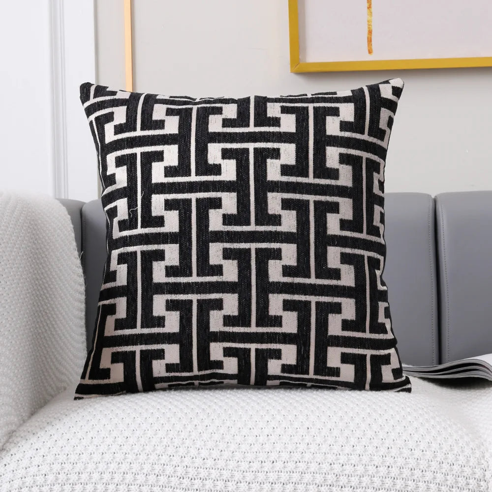 A black and off-white geometric patterned lumbar pillow cover resting on a gray sofa.