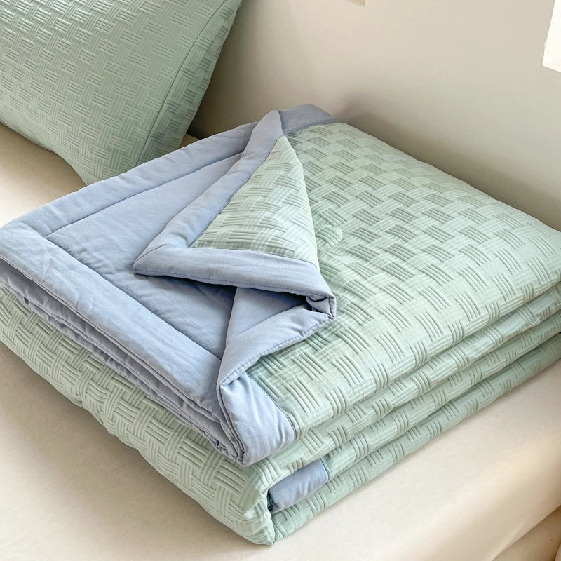 A stack of breathable waffle quilts in light sage green and pale blue fabric.