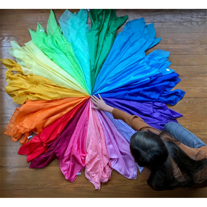 A vibrant fan of rainbow-colored silk scarves spread out on a wooden floor.