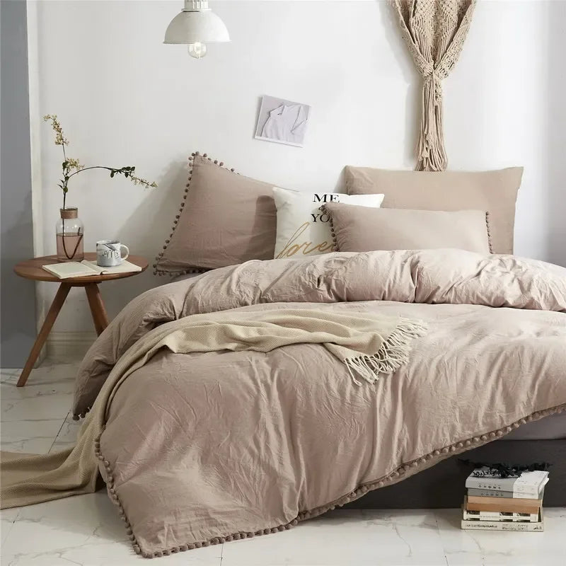 A beige duvet cover set with pom-pom decoration displayed on a bed in a bright room.