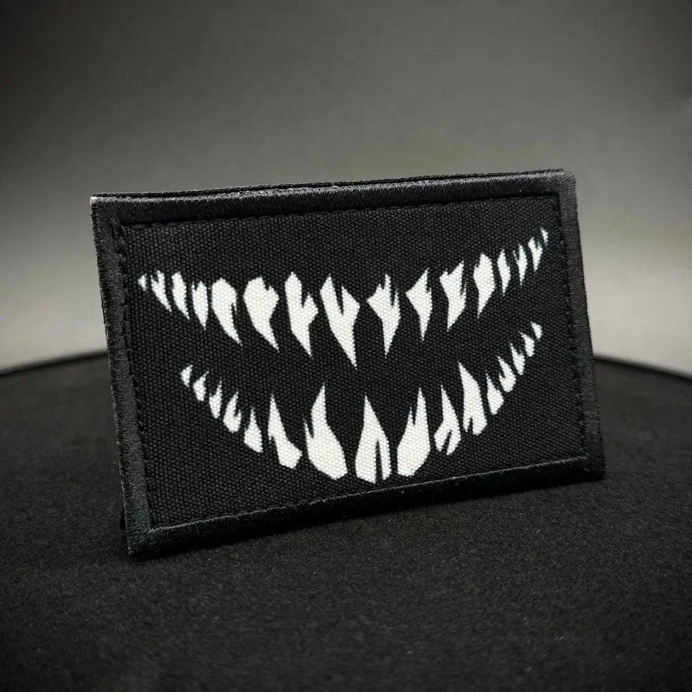 A black rectangular patch featuring a white design of stylized teeth or fangs.