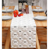 A festive Halloween table runner with a white textured fabric and black ghost patterns set on a wooden table.