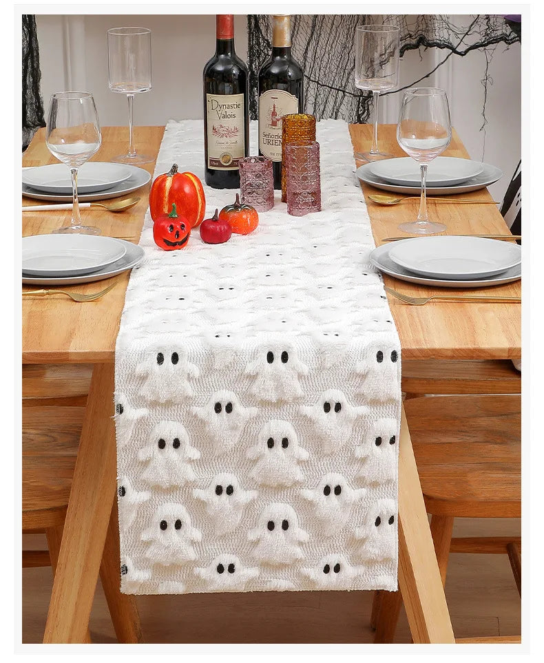 A festive Halloween table runner with a white textured fabric and black ghost patterns set on a wooden table.