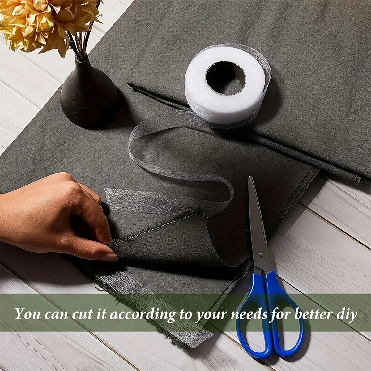 A hand is cutting a piece of gray fabric using scissors on a dark gray mat, with a roll of white tape nearby.