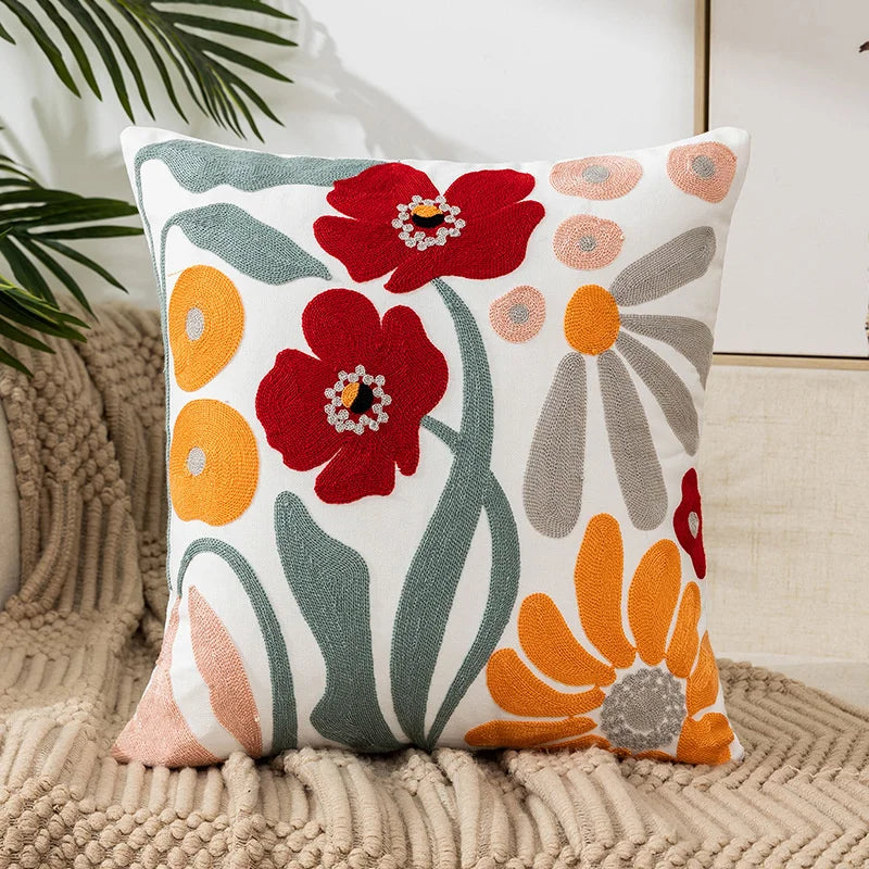 A throw pillow cover featuring embroidered red and orange floral designs on a white background.