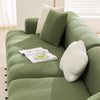 A light green stretchable full-wrap sofa slipcover with white accent pillows and a cup on the seat.