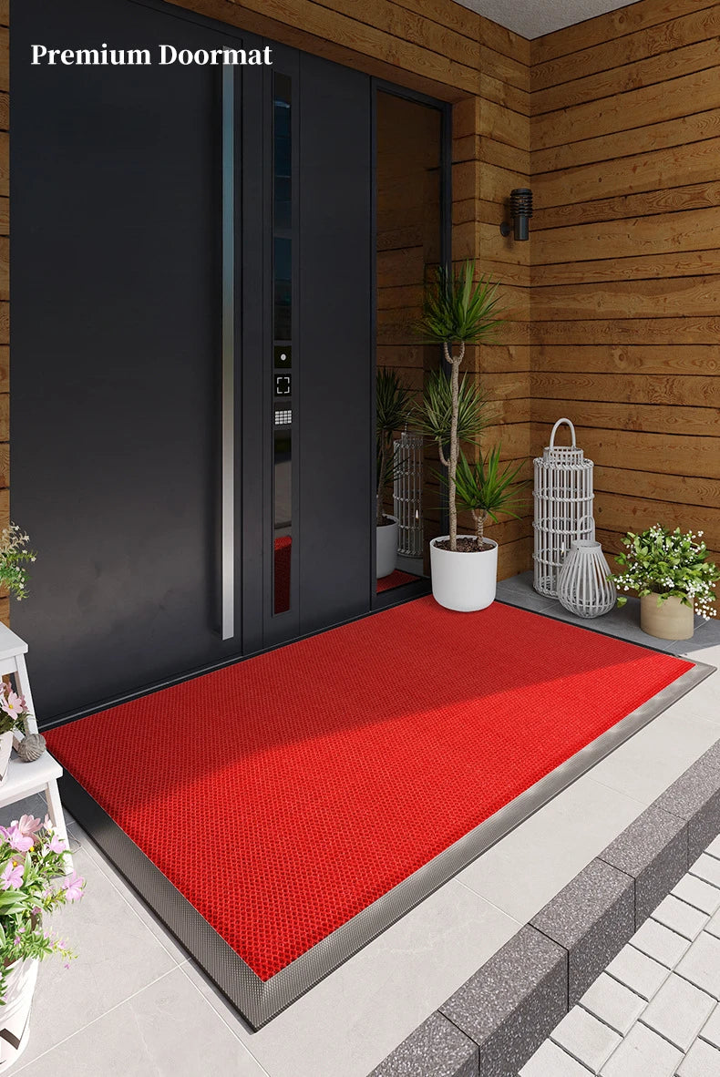 A red non-slip rubber doormat placed on a gray tiled floor in front of a dark wooden door.