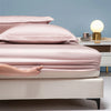 A close-up of a luxury bamboo bedding set featuring soft pink and cream colored sheets and pillows on a bed.