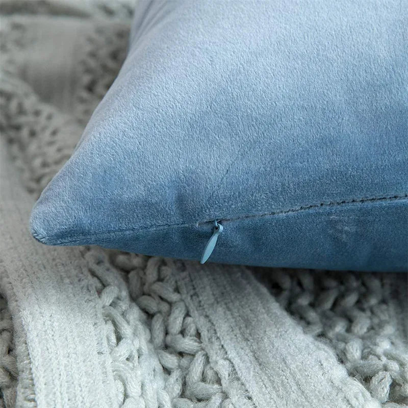 A close-up of a soft blue velvet decorative pillow cover resting on a knitted gray fabric.