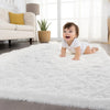 A baby lying on a fluffy white carpet in a bright room with a sofa and potted plant visible.